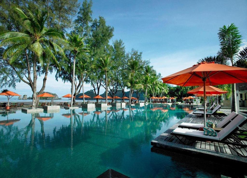 Resort swimming pool with palm trees and orange umbrellas over lounge chairs