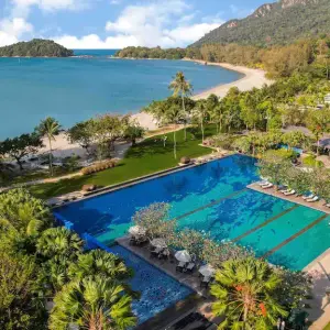 A large outdoor swimming pool at a beach resort with tropical trees and a sandy beach nearby