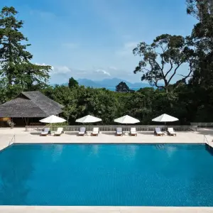 Swimming pool with white umbrellas and lounge chairs surrounded by trees and blue sky