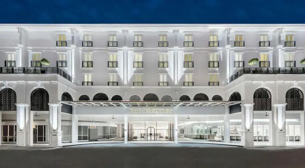 White illuminated hotel façade with balconies and main entrance at night