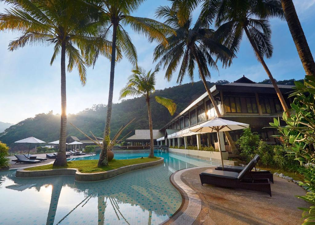 Resort pool with palm trees, sun loungers, umbrellas, hotel building, and hills