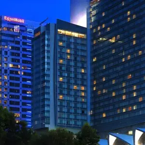 High-rise hotel and office buildings lit up at dusk with trees in foreground