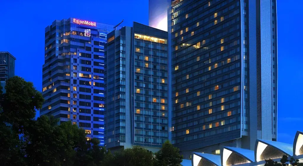 High-rise hotel and office buildings lit up at dusk with trees in foreground